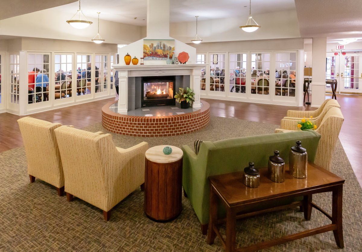 A cozy lounge with comfortable seating arranged around a central fireplace.