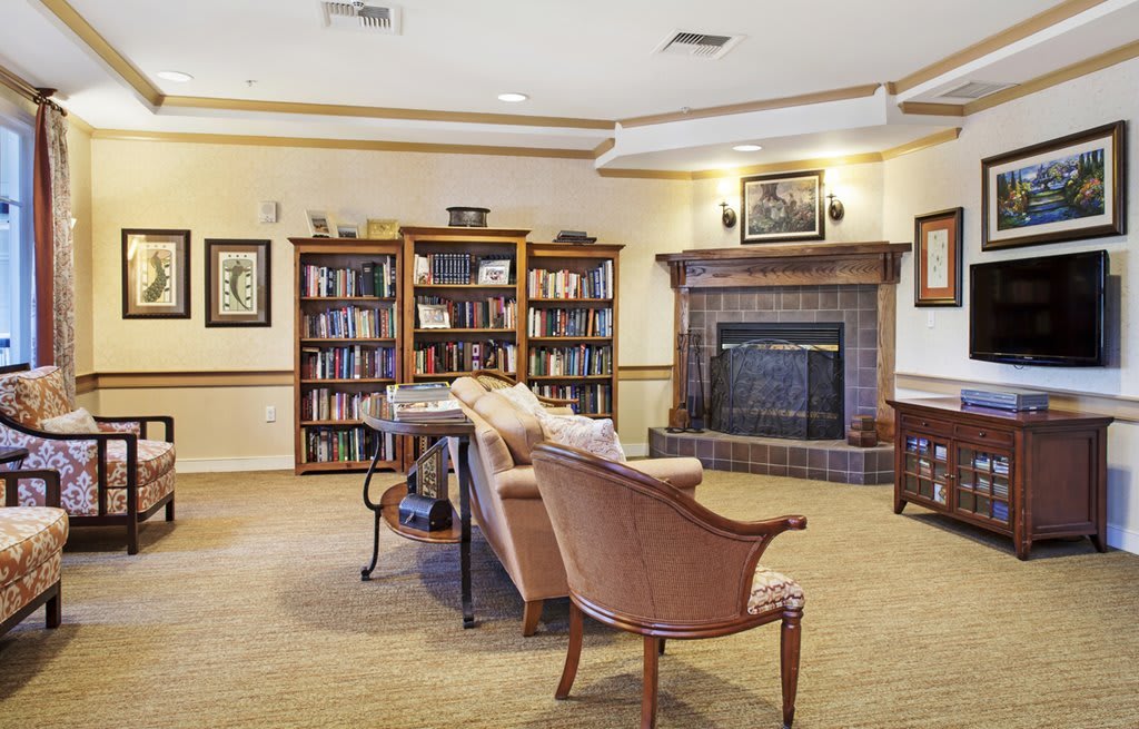 A cozy library room with bookshelves, a fireplace, and comfortable seating.