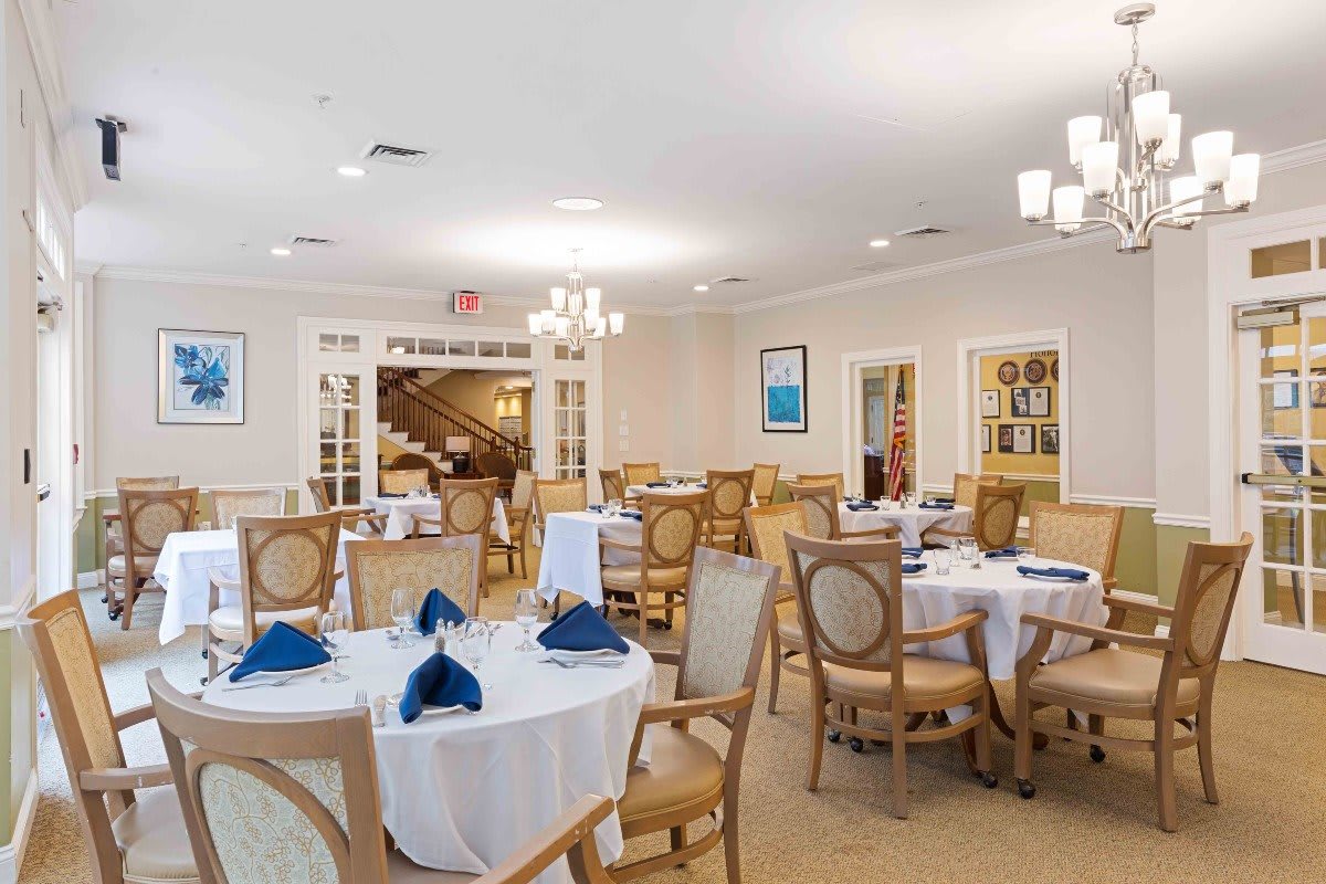 A well-lit dining area with round tables set with white tablecloths and blue napkins.
