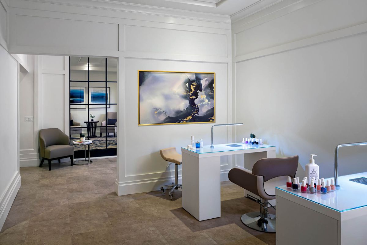 A modern nail salon interior featuring stylish furniture and a large piece of abstract artwork on the wall.