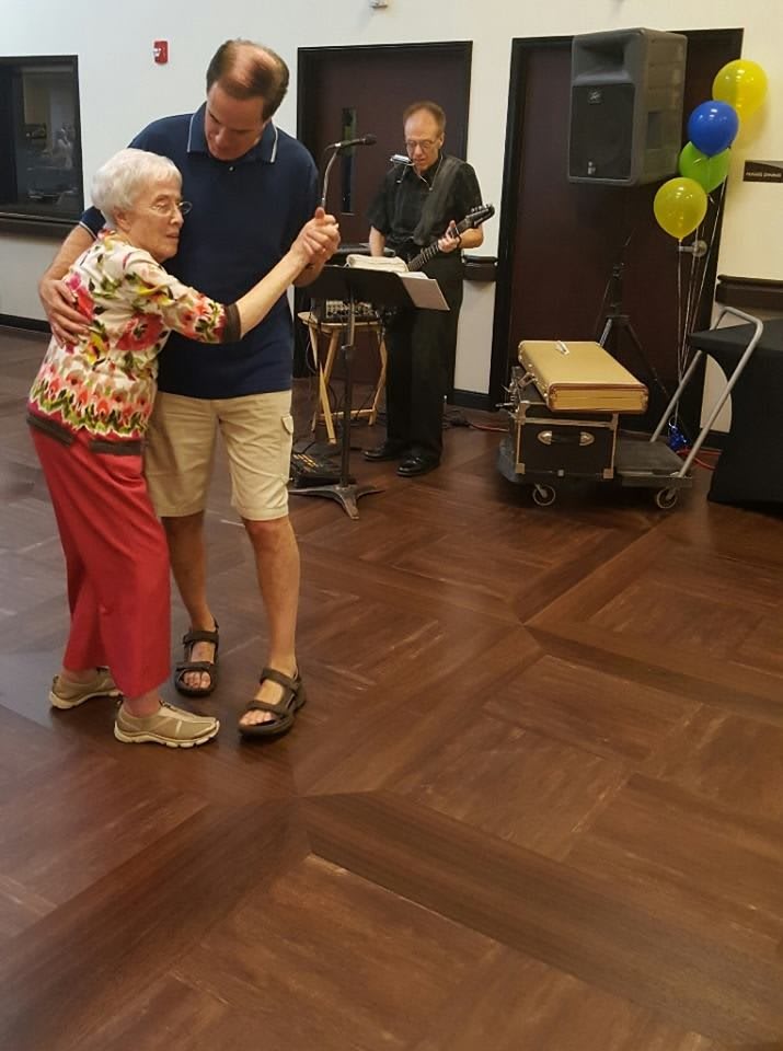 An elderly woman and a man dance together as a live band plays music in the background.