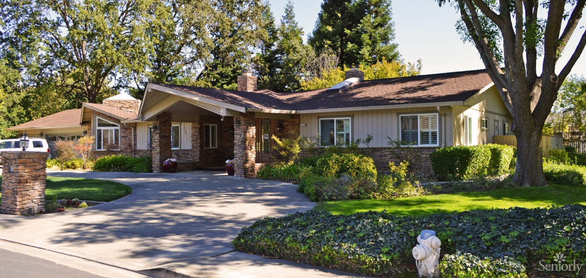 A cozy residential house with a driveway and lush garden surrounded by trees.