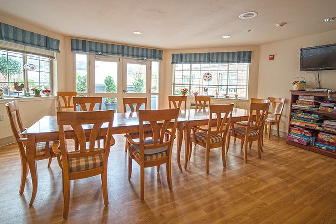 A spacious dining room with wooden tables and chairs, featuring large windows that let in natural light.