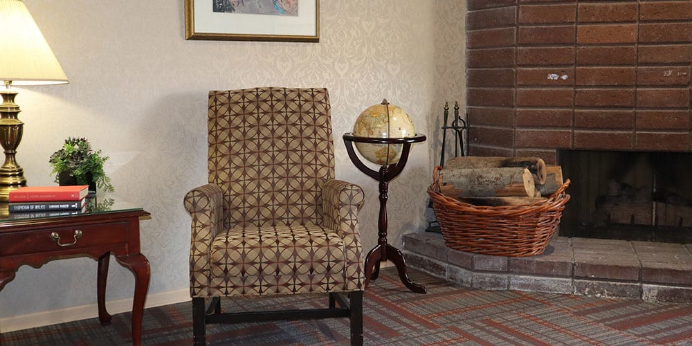 A cozy living room corner featuring an armchair, a globe on a stand, and a fireplace with baskets beside it.