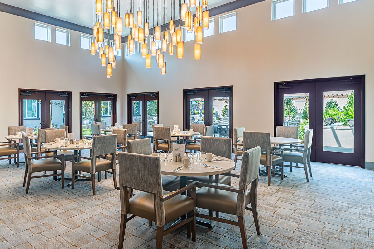 A well-lit dining area with arranged tables and chairs under modern chandeliers.