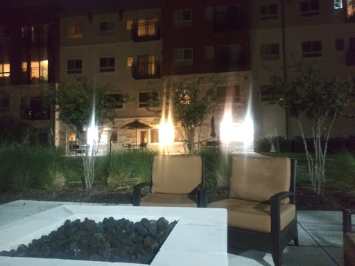 A cozy outdoor seating area with chairs around a fire pit, set against the backdrop of an apartment complex at night.