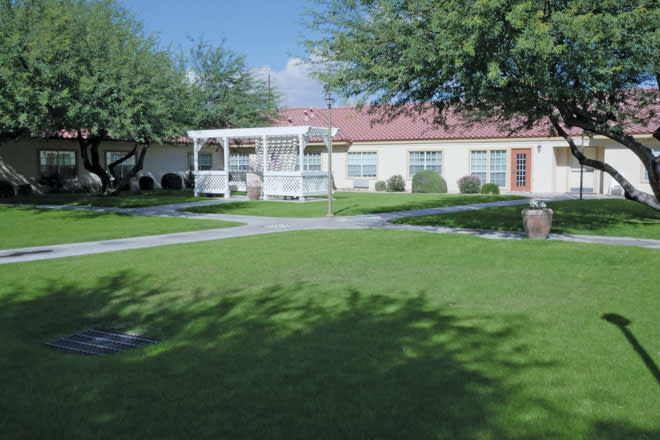 A sunny outdoor area with a well-maintained lawn and a gazebo in front of a building.