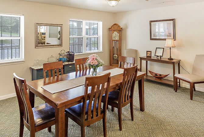 A cozy dining room with wooden furniture, including a table and chairs, decorated with a grandfather clock and fresh flowers.