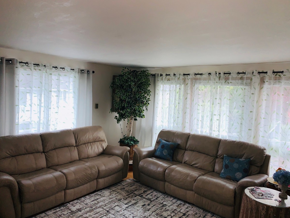 A cozy living room with two brown sofas, a patterned rug, and large windows adorned with white curtains.