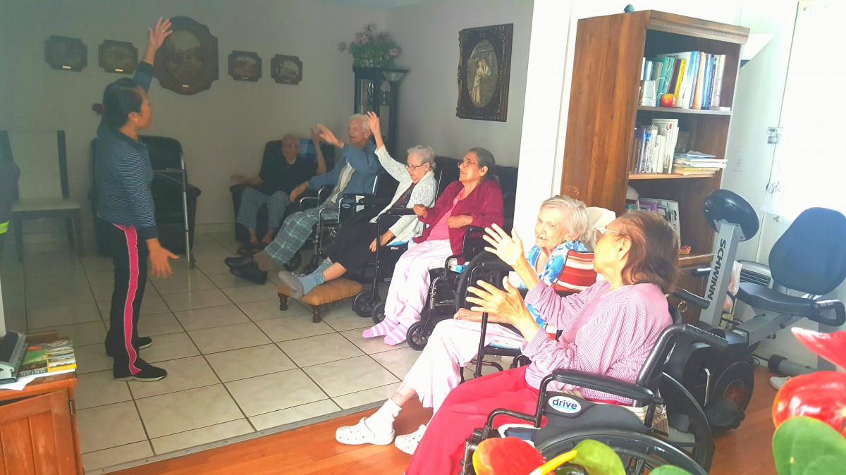 A group of elderly people engaged in an activity indoors, some using wheelchairs.