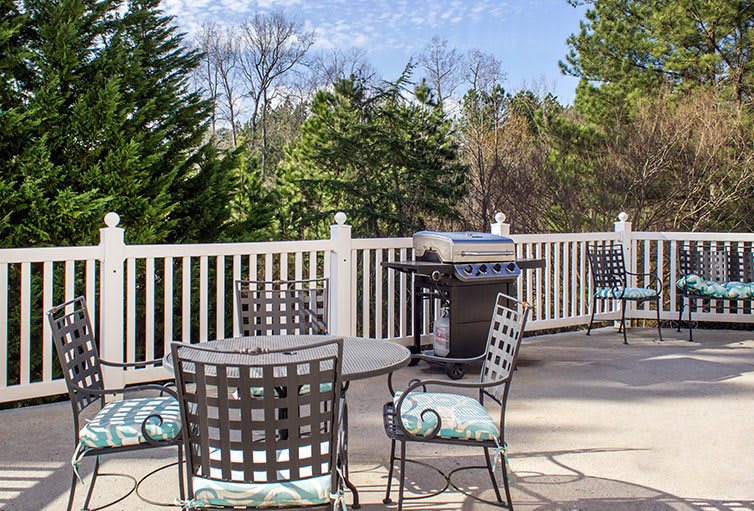 A cozy outdoor patio with metal furniture and a grill, surrounded by nature.