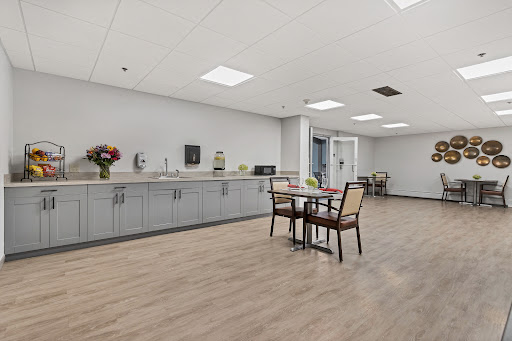 A modern break room featuring a kitchenette, table, and chairs, decorated with flowers.