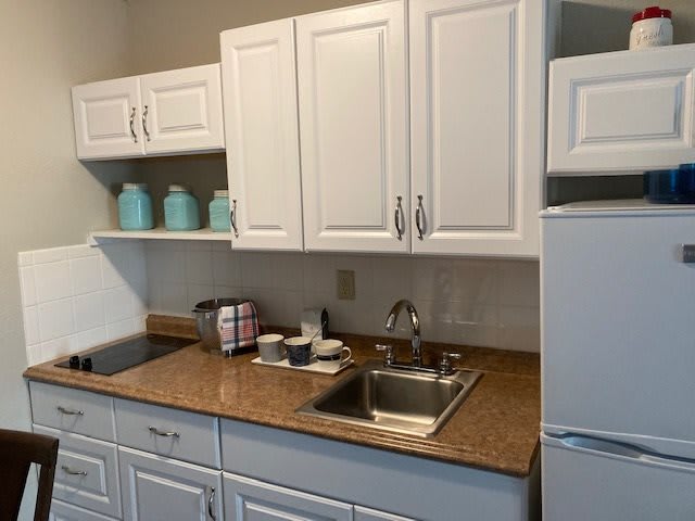 A compact kitchen with white cabinets, a countertop, sink, and fridge.