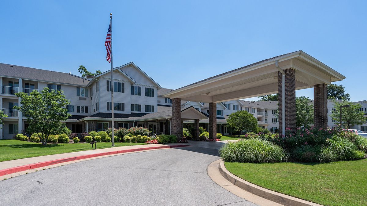 A view of a building entrance with a driveway and landscaping under a clear blue sky.