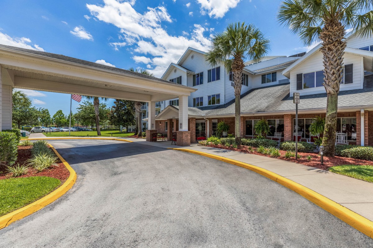 A building entrance with a covered driveway and landscaped surroundings on a sunny day.