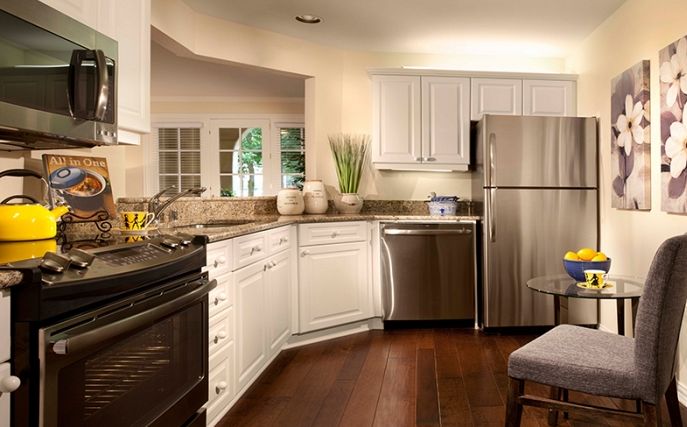 A modern kitchen featuring stainless steel appliances and white cabinetry with wood flooring.