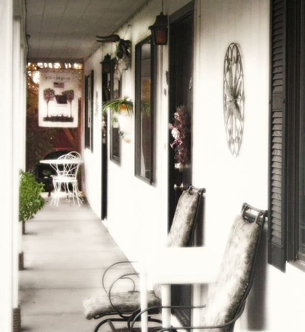 A cozy porch area with chairs and a table along an outdoor corridor.