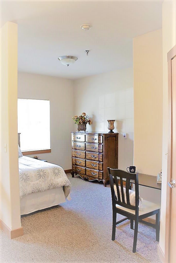 A cozy bedroom with a bed, dresser, and chair by the window.