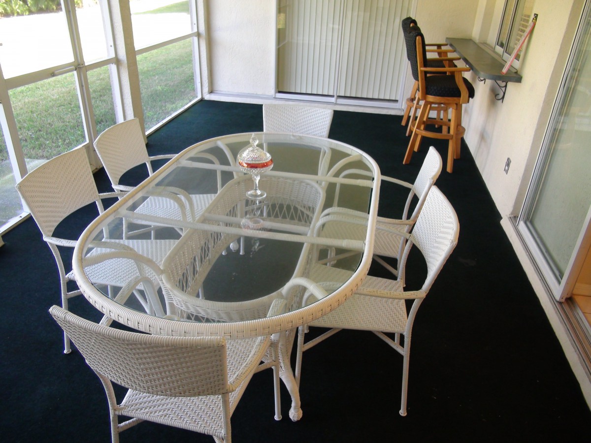 A cozy dining area with a glass table, surrounded by wicker chairs and adjacent to a counter with bar stools.