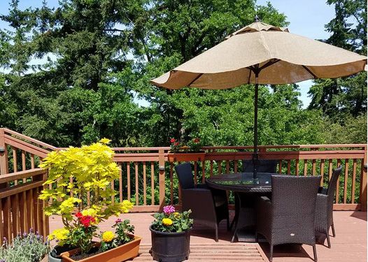 A sunny patio with outdoor seating and a large umbrella surrounded by vibrant flowers and lush greenery.