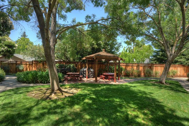 A peaceful garden setting with a gazebo and picnic tables under the shade of tall trees.