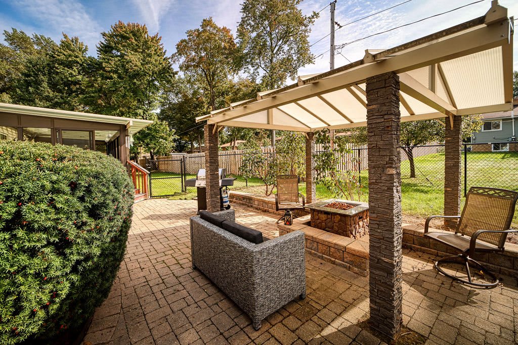 A beautiful outdoor patio area featuring comfortable seating under a pergola in a well-maintained backyard.