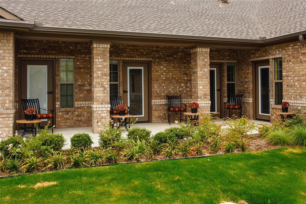 A brick house with a porch featuring columns and landscaping including plants and grass.