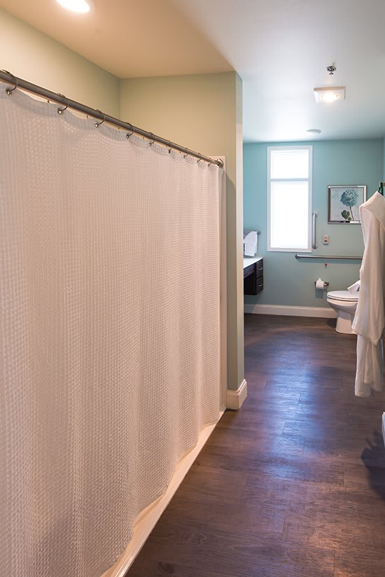 A clean and spacious bathroom featuring a shower curtain, toilet, sink, and mirror with natural light from a window.