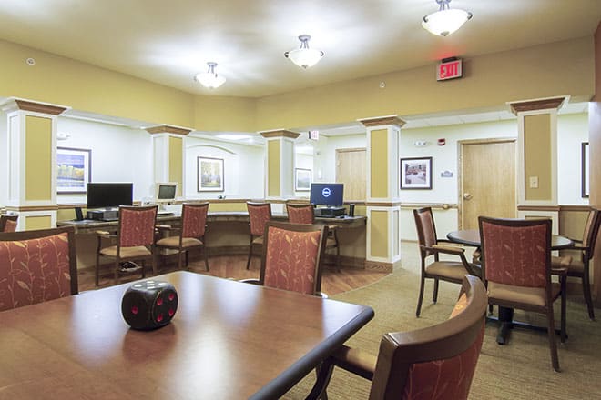 A spacious room with chairs, tables, and computers, featuring warm lighting.