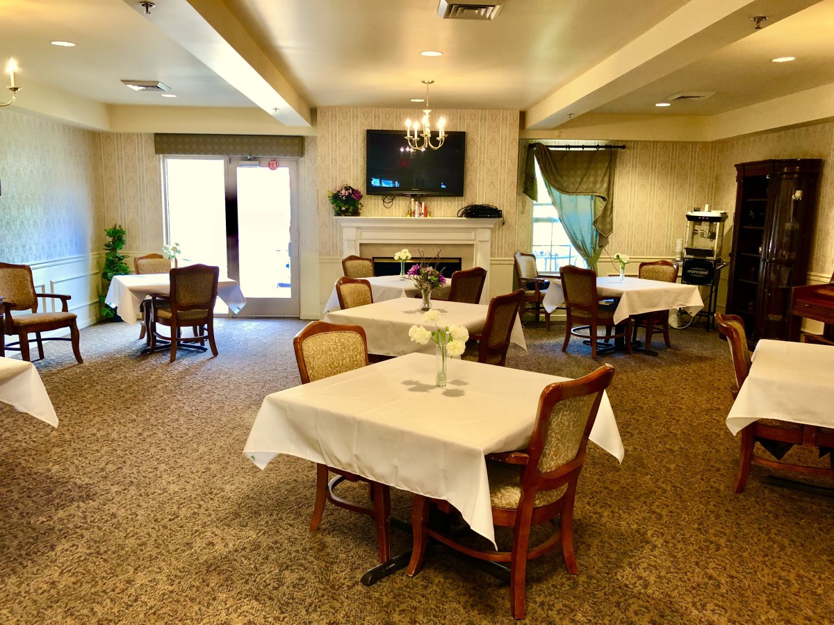 A cozy dining area with tables covered in white tablecloths, set around a fireplace and television.
