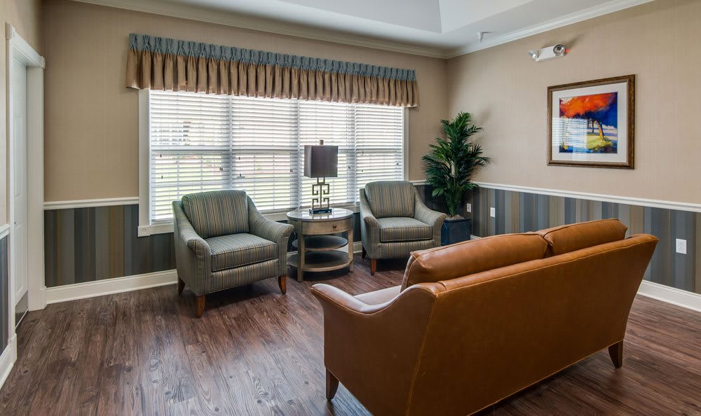 A cozy living room with a sofa, two chairs, a side table, and a lamp by the window.