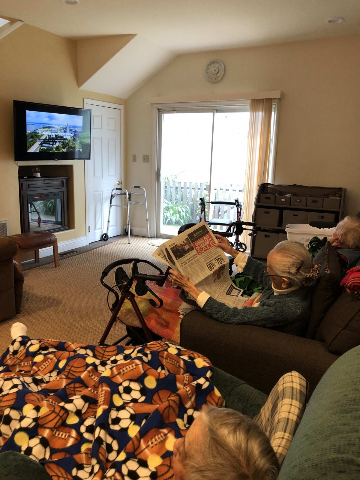 An elderly person reading a magazine in a cozy living room with a television on.