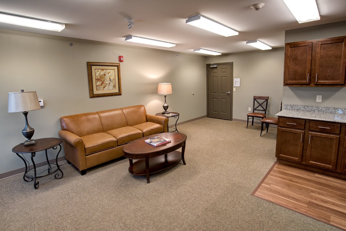 A cozy living room with a brown leather sofa, a wooden coffee table, and a floor lamp under bright ceiling lights.