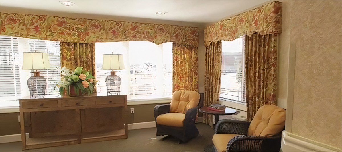 A cozy living room with armchairs, a lamp, and decorative curtains.