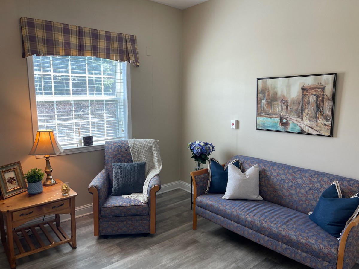 A cozy living room with a sofa, armchair, and artwork on the wall.
