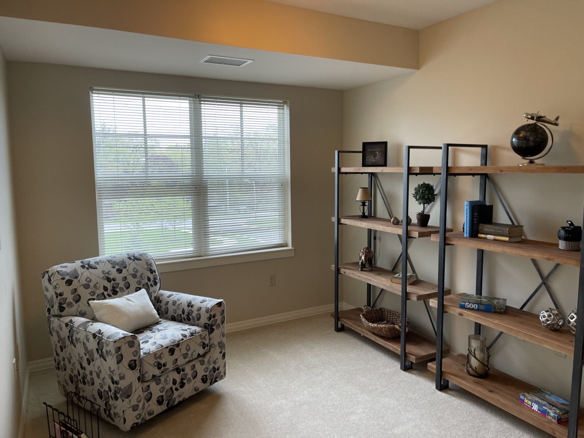 A cozy living room with an armchair, bookshelf, and large window.