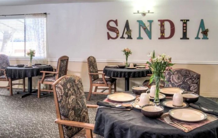 A cozy dining room setup with elegantly arranged tables and chairs, featuring floral centerpieces and decorative wall art.