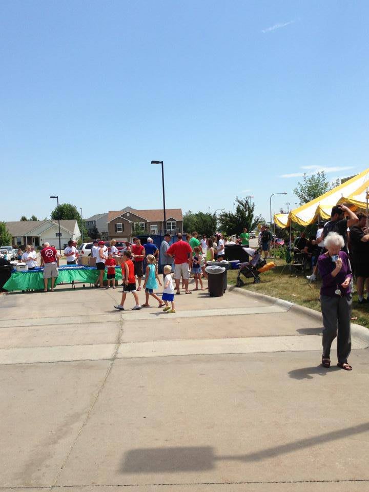 A community event with people gathered around tents on a sunny day.