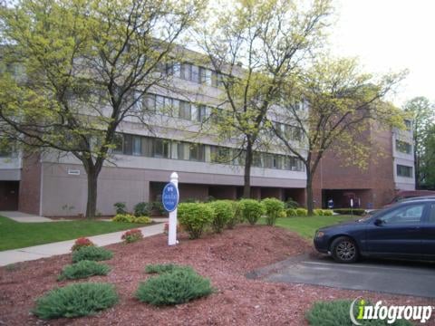 A four-story building surrounded by trees and landscaping with a car parked in front.