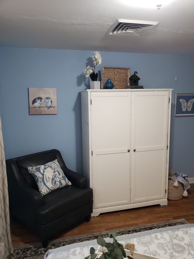 A cozy living room corner with a white wardrobe, black armchair, and decorative artwork on blue walls.