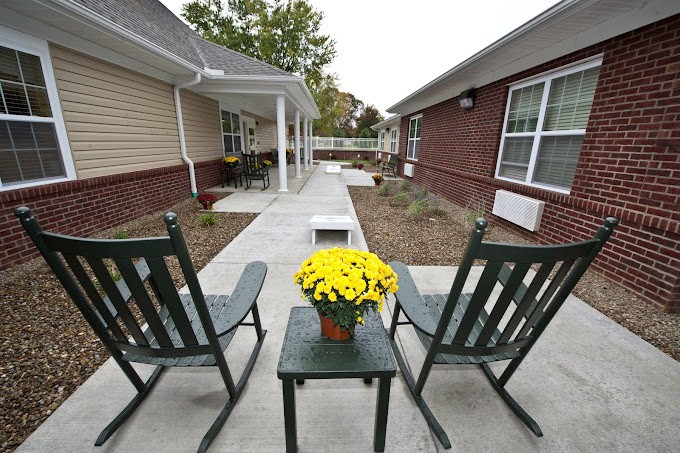A peaceful patio area with two chairs, a small table, and a potted plant overlooking a walkway between buildings.