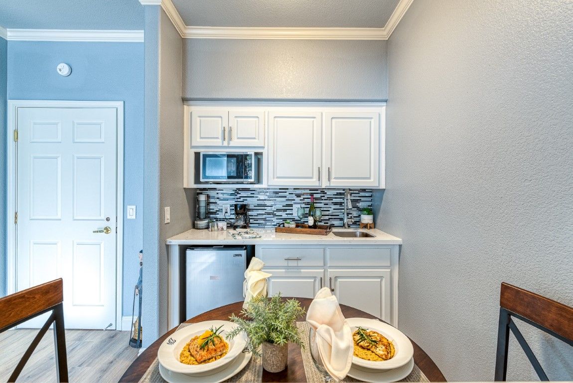 A modern and compact kitchen with white cabinets, a small dining table set for two, and stylish decor.