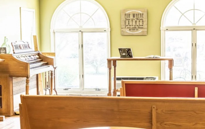 A peaceful church interior featuring wooden pews, an organ, and large arched windows.