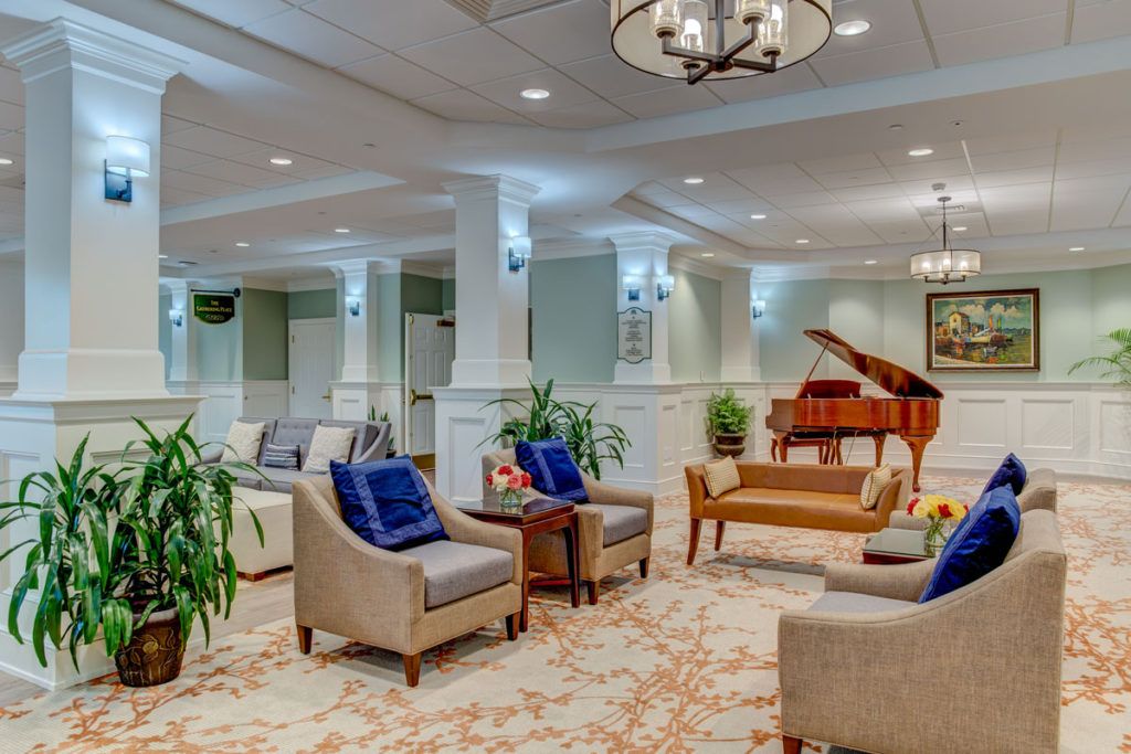 A spacious lounge featuring comfortable seating, a grand piano, elegant lighting, and lush plants.