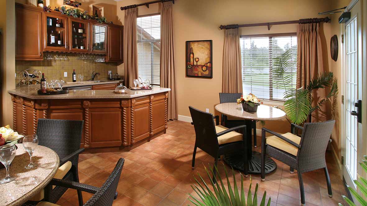 A cozy kitchen and dining area with wooden cabinets, a round table, and large windows providing natural light.