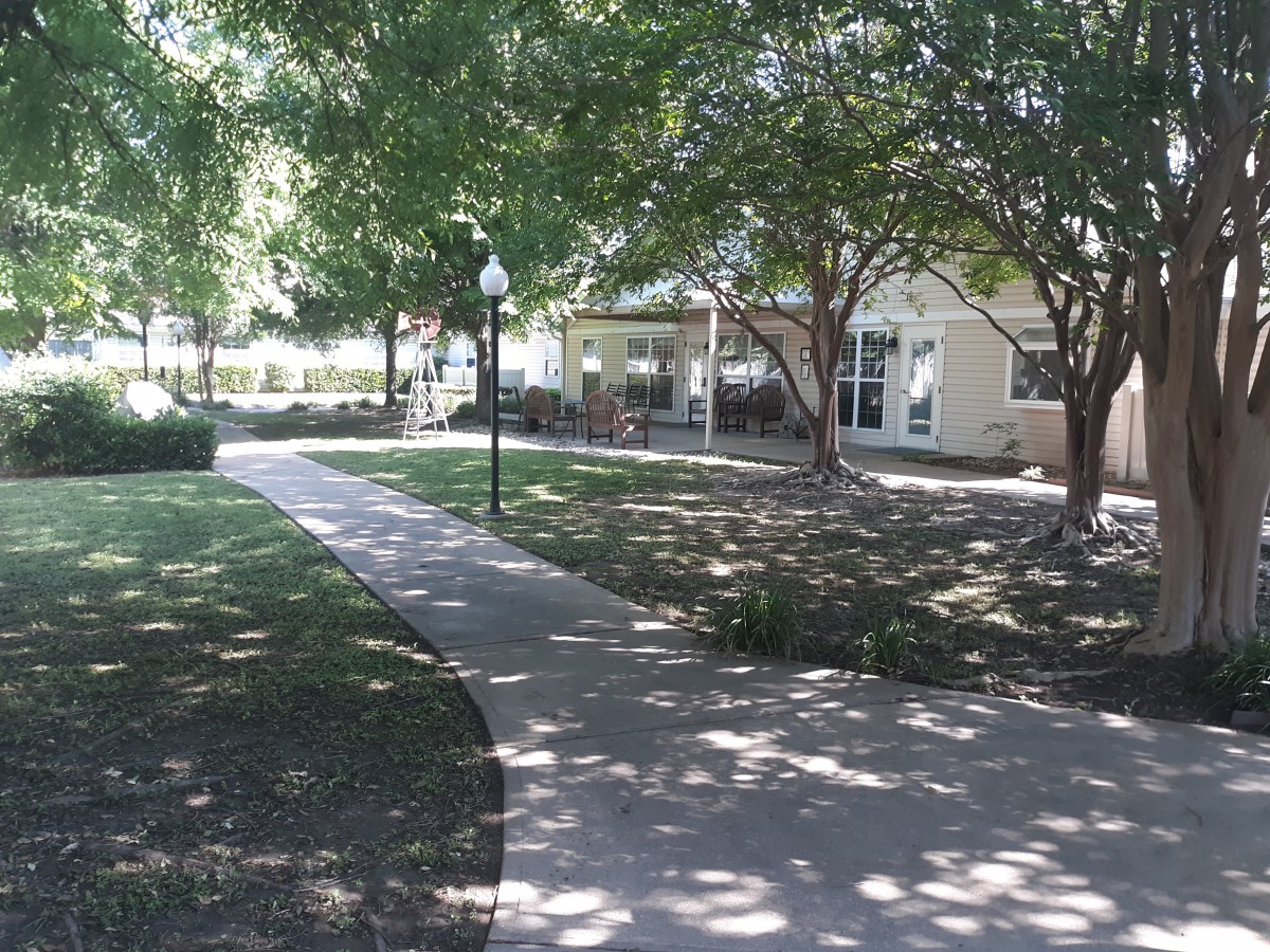 A peaceful park scene with a sidewalk leading to a building, surrounded by trees and greenery.