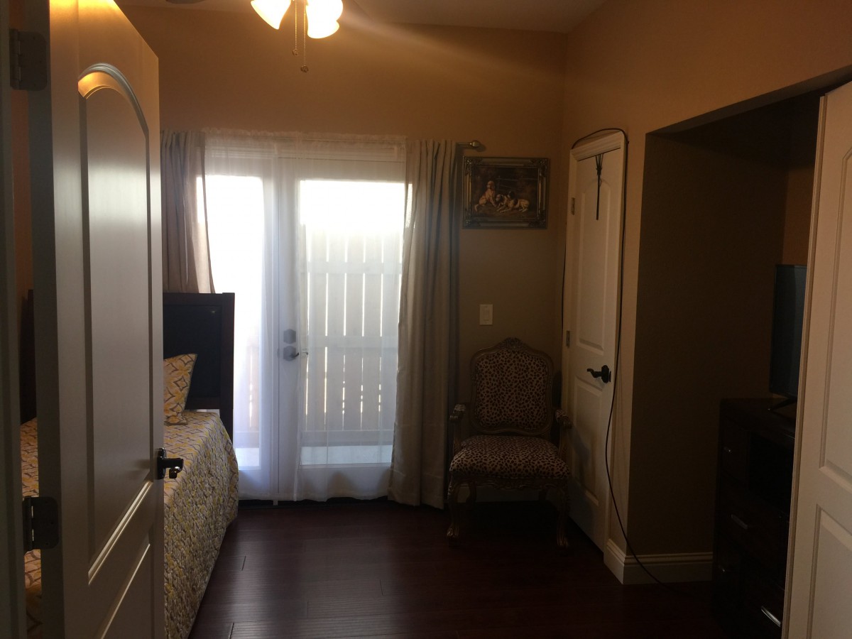 A cozy bedroom with a door leading outside, featuring curtains, a chair, and soft lighting.