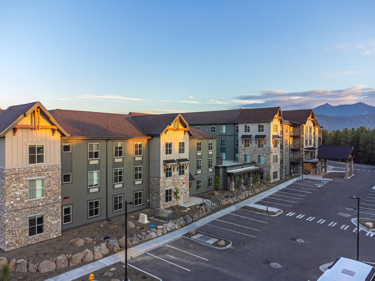 A modern hotel building with a parking lot, set against a mountainous landscape at sunset.