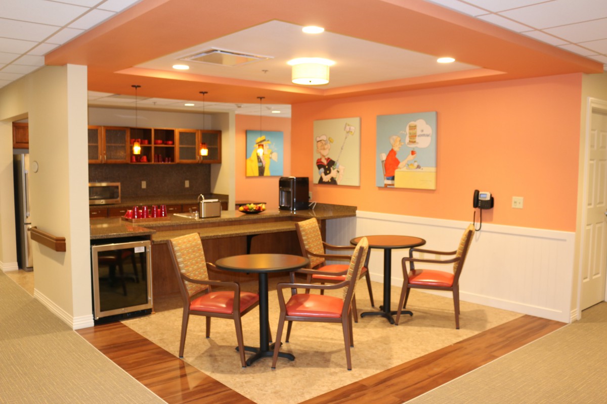 A cozy cafe interior with tables, chairs, and colorful artwork on orange walls.