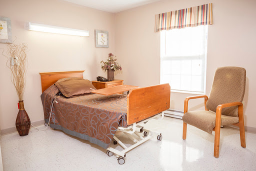 A well-lit hospital patient room featuring an adjustable bed, a chair, and natural light coming in through the window.